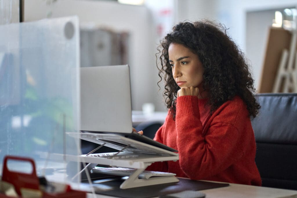 Busy latin female worker working on laptop thinking analyzing online data.